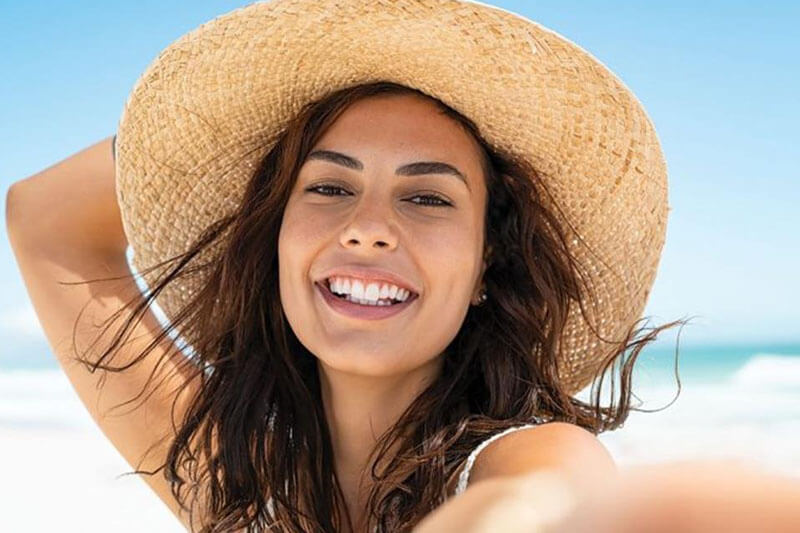Picture of a on the beach, happy with her plastic surgery at Top Plastic Surgeons in the U.K.  The woman is wearing tan sun hat and sitting on a Costa Rica beach.