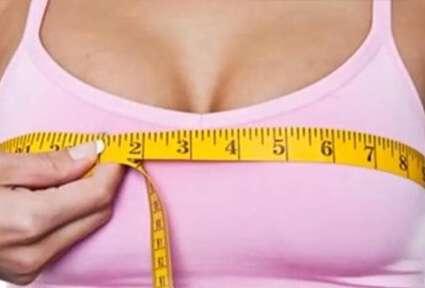 Picture of a woman measuring her breasts with a tape measure, and happy with the perfect breast reduction procedure she had at Top Plastic Surgeons in beautiful San Jose, Costa Rica.  She is wearing a light purple top and facing the camera.