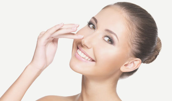 Picture of a woman, facing the camera and happy with her perfect nose surgery procedure she had at Top Plastic Surgeons in beautiful San Jose, Costa Rica.  The woman has her hand to the side of her nose and is pointing to where she had the surgery.